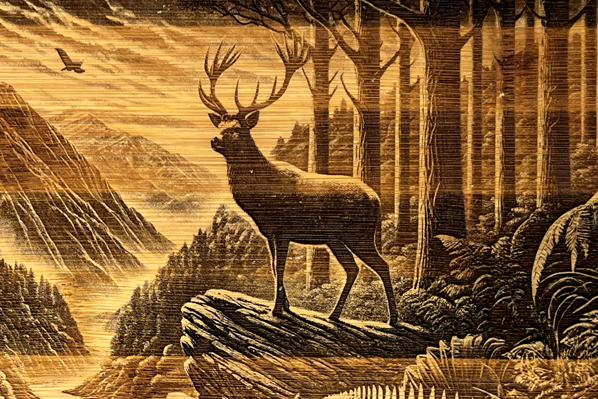 Close-up of the Stag’s Edge wooden board engraving, showing a stag on a rocky ledge, forest, mountain valley and the natural wood grain.